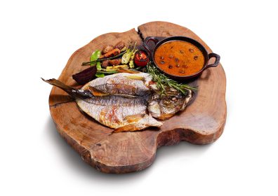 O robalo é assado e servido com molho puttanesca feito com tomate, alcaparras, azeitonas pretas e vinho branco. Como acompanhamento, legumes orgânicos típicos do verão.